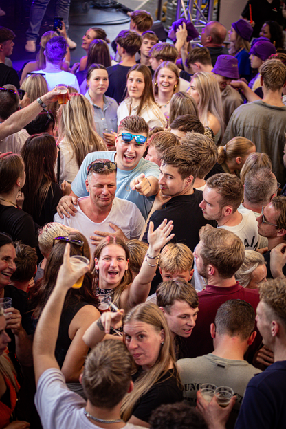 A big crowd of people, one wearing a shirt that reads "Slinger", is seen at an event.