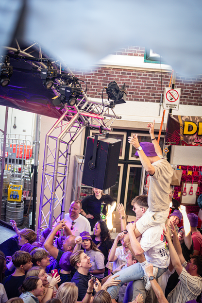 A lively concert scene with a group of people standing together and one person being lifted into the air.