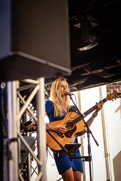 A blonde woman in a blue dress holds a guitar on stage.