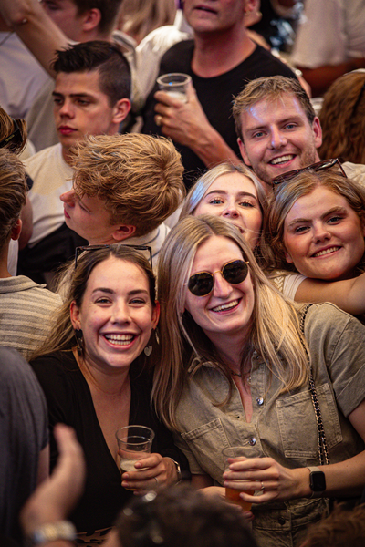 A woman is surrounded by a group of smiling people, and she is wearing sunglasses.