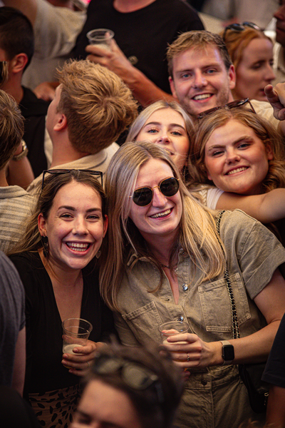 A group of people are standing close together, smiling and laughing. The scene is lively and filled with joy.