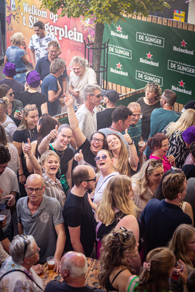 A lively scene of a group of people standing together, enjoying the atmosphere in front of a sign that says "Slinger".