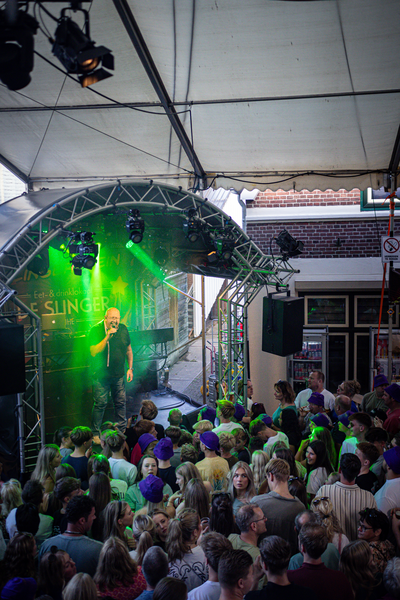 A group of people, including some wearing purple hats, are gathered around a stage for a concert.