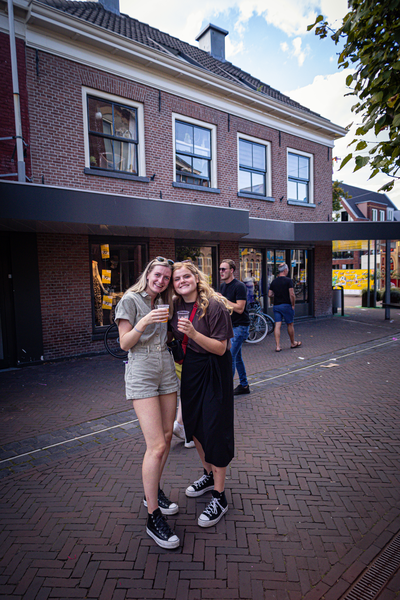 Two girls pose for a picture on a sidewalk in front of the Diekdaegen building.