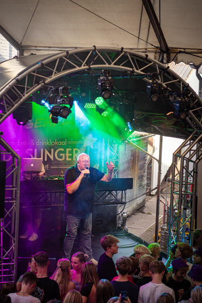 A singer on stage with a purple and green light display behind him at Slinger Zondag.