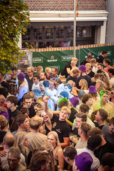 A group of people stand in front of a green sign that says "slinger zondag".