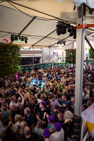 A large crowd of people are gathered under a tent with an orange sign that says "Slinger".