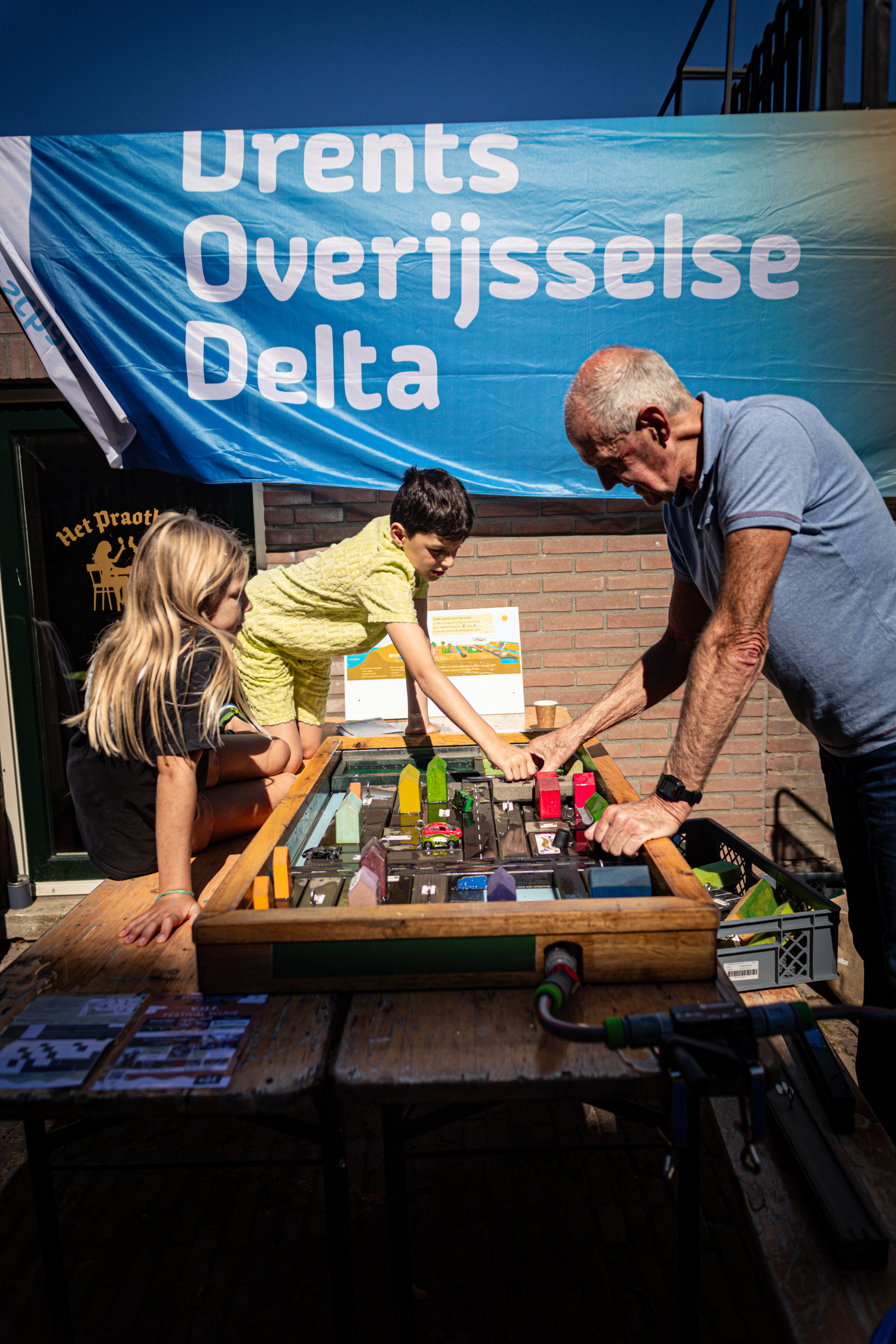A group of people are around a table with lots of electronics. There is a sign that says "Drents Overijse Delta".