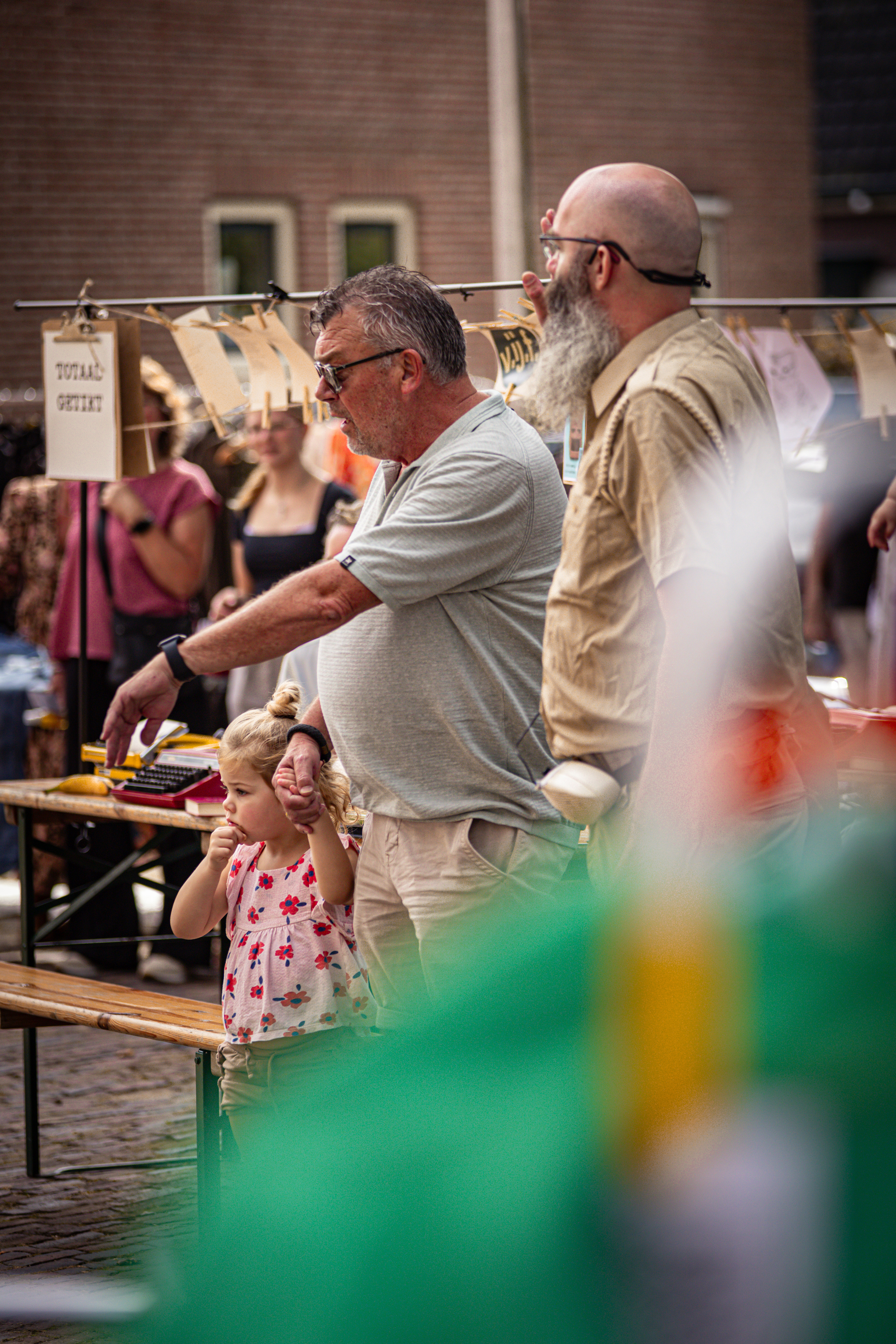 A group of people at a public event, with a man holding a sign that says "Jus" and a child sitting on his shoulder.