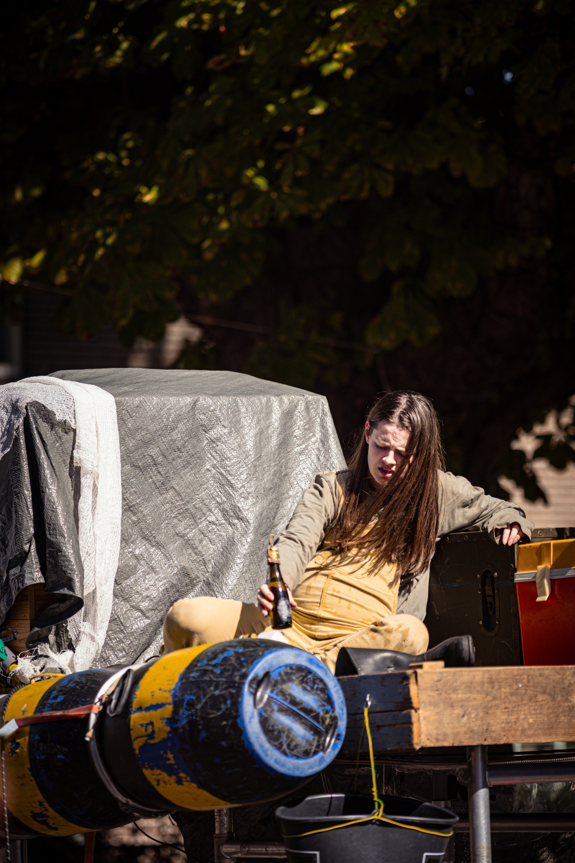 A woman in a yellow shirt and jeans sits on the floor near some musical instruments.