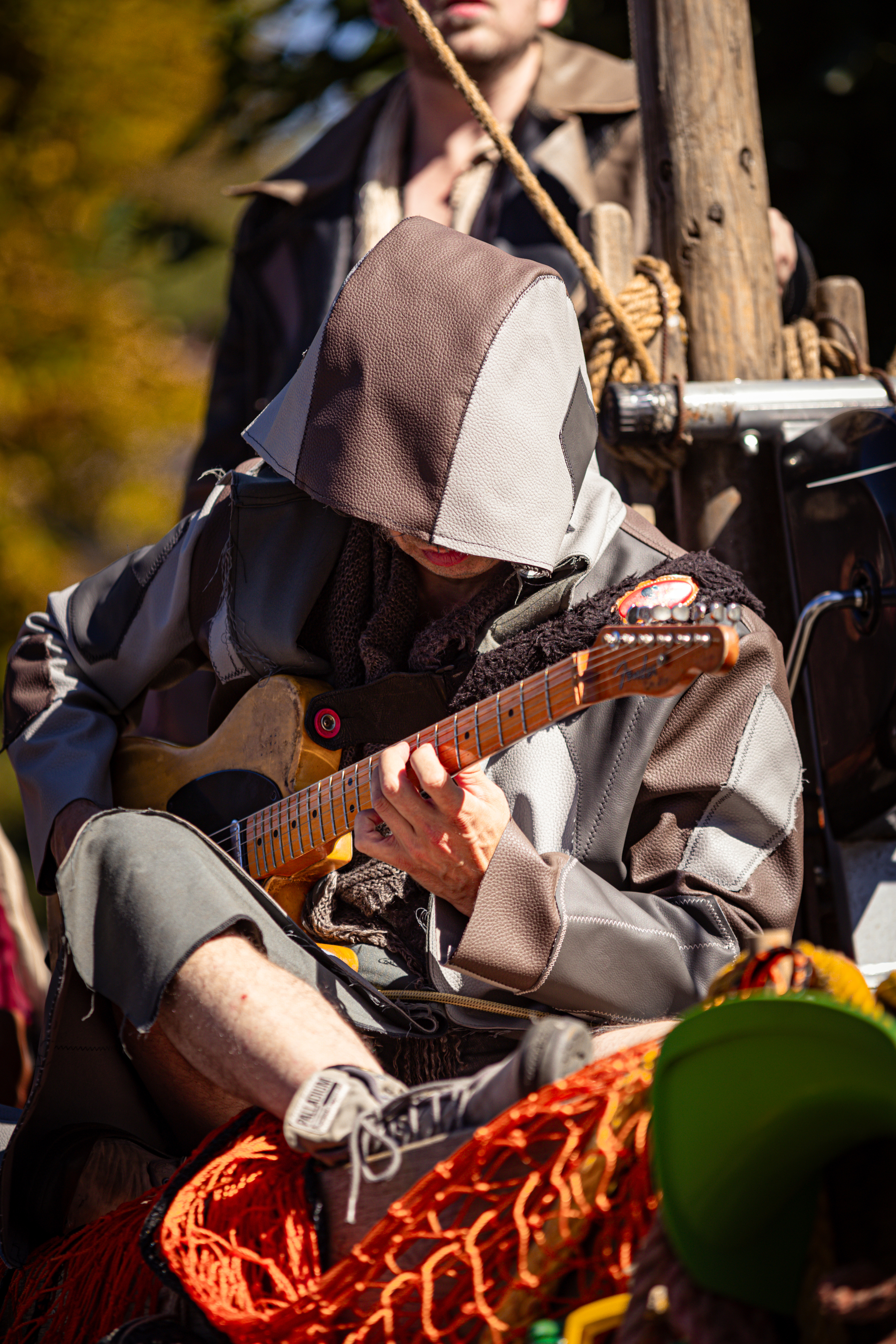 A man in a grey hooded jacket plays guitar with the brand name "Schonbrun" on his sleeve.