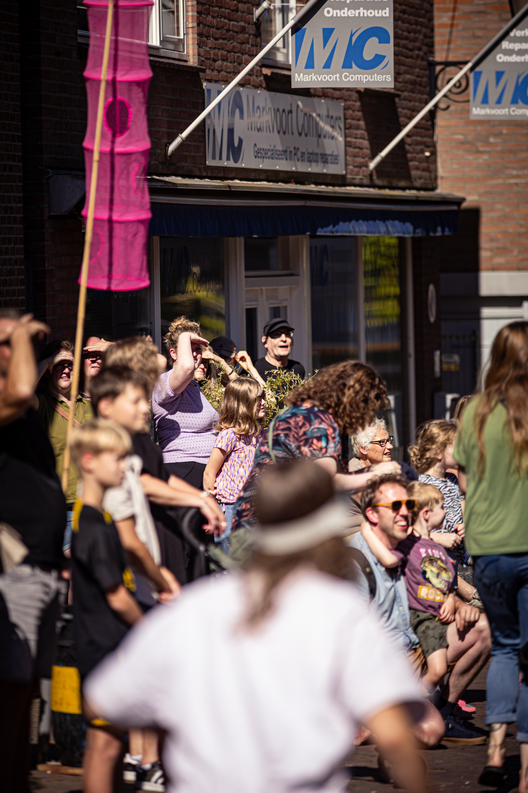 A family is seen taking a picture outside the V.IJ.F. Festival venue, which has red brick walls and blue and white signs.