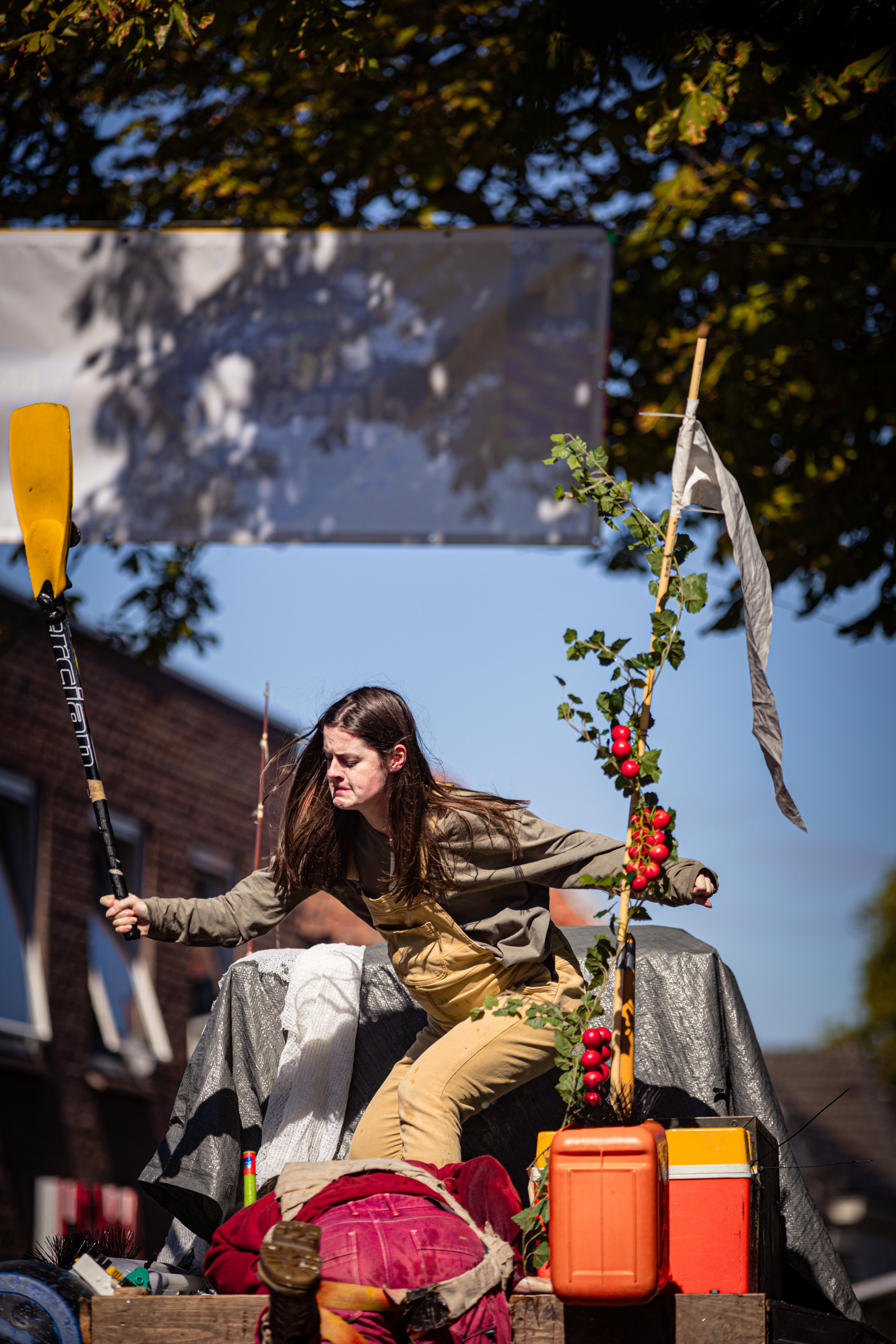 A woman in a tan jacket is holding a yellow paddle and standing behind an orange bucket at the V.I.J. Festival.