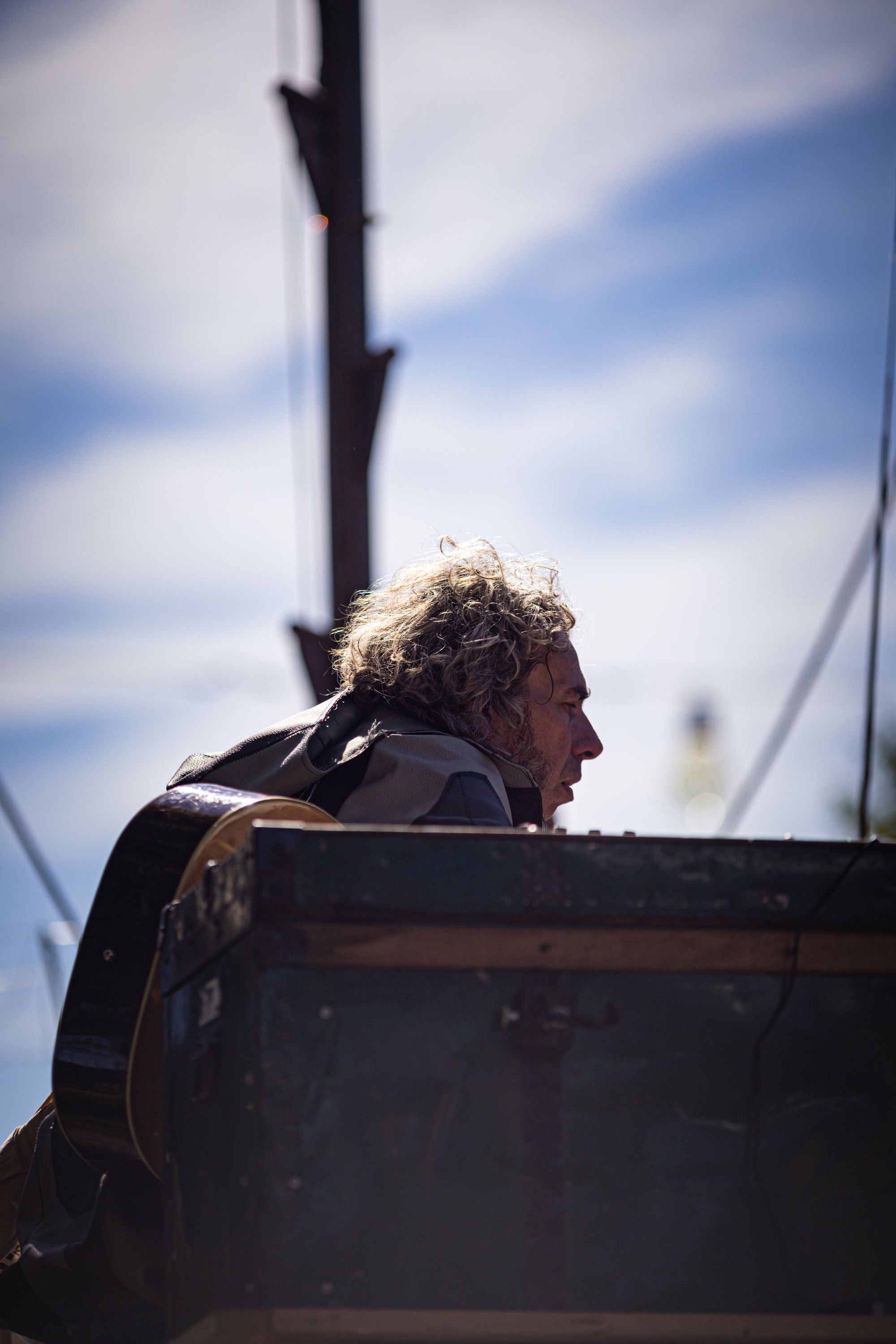 A man sitting on a blue stool holding a guitar with his head down.