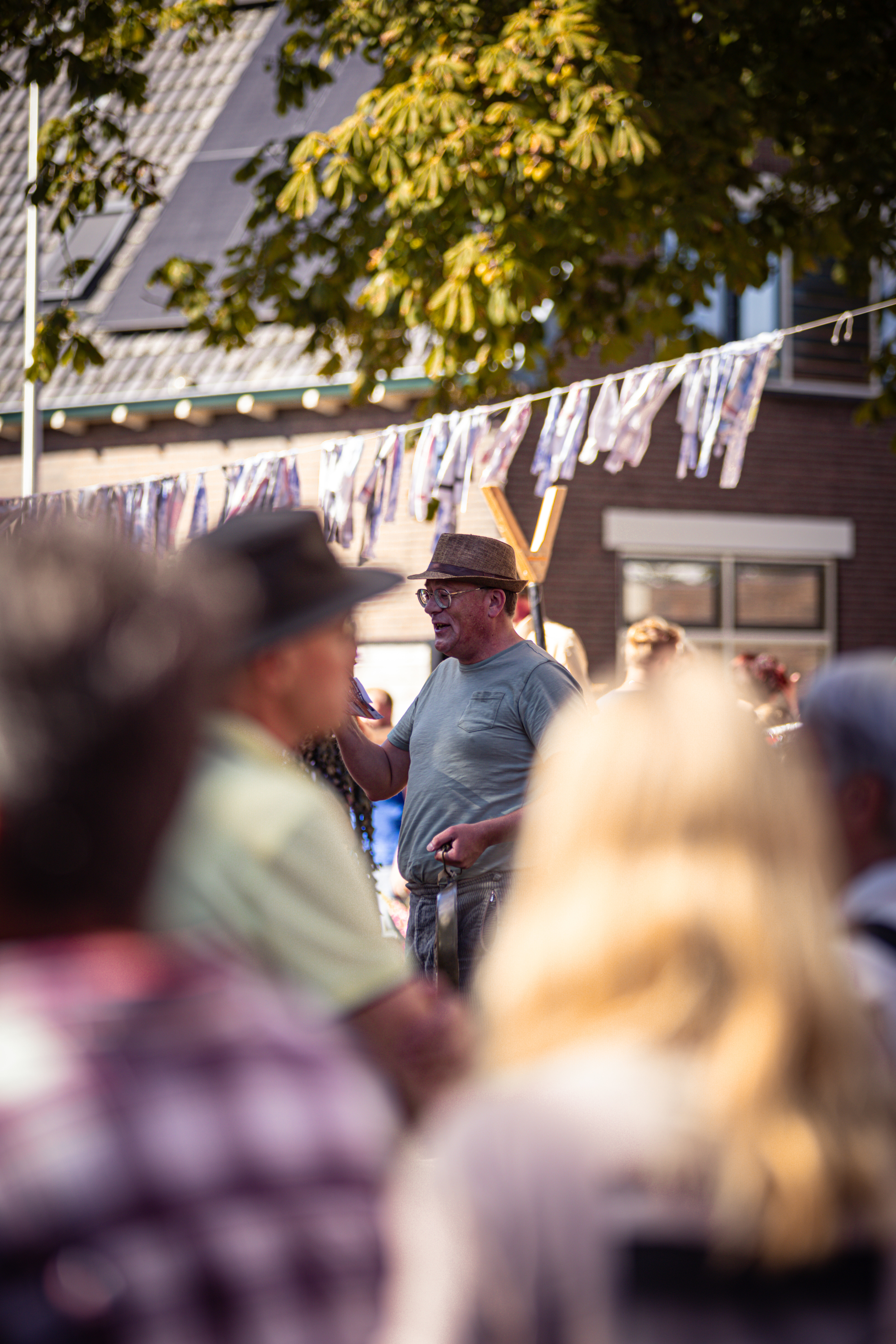 A man with a hat and glasses is speaking to the crowd at an outdoor event.