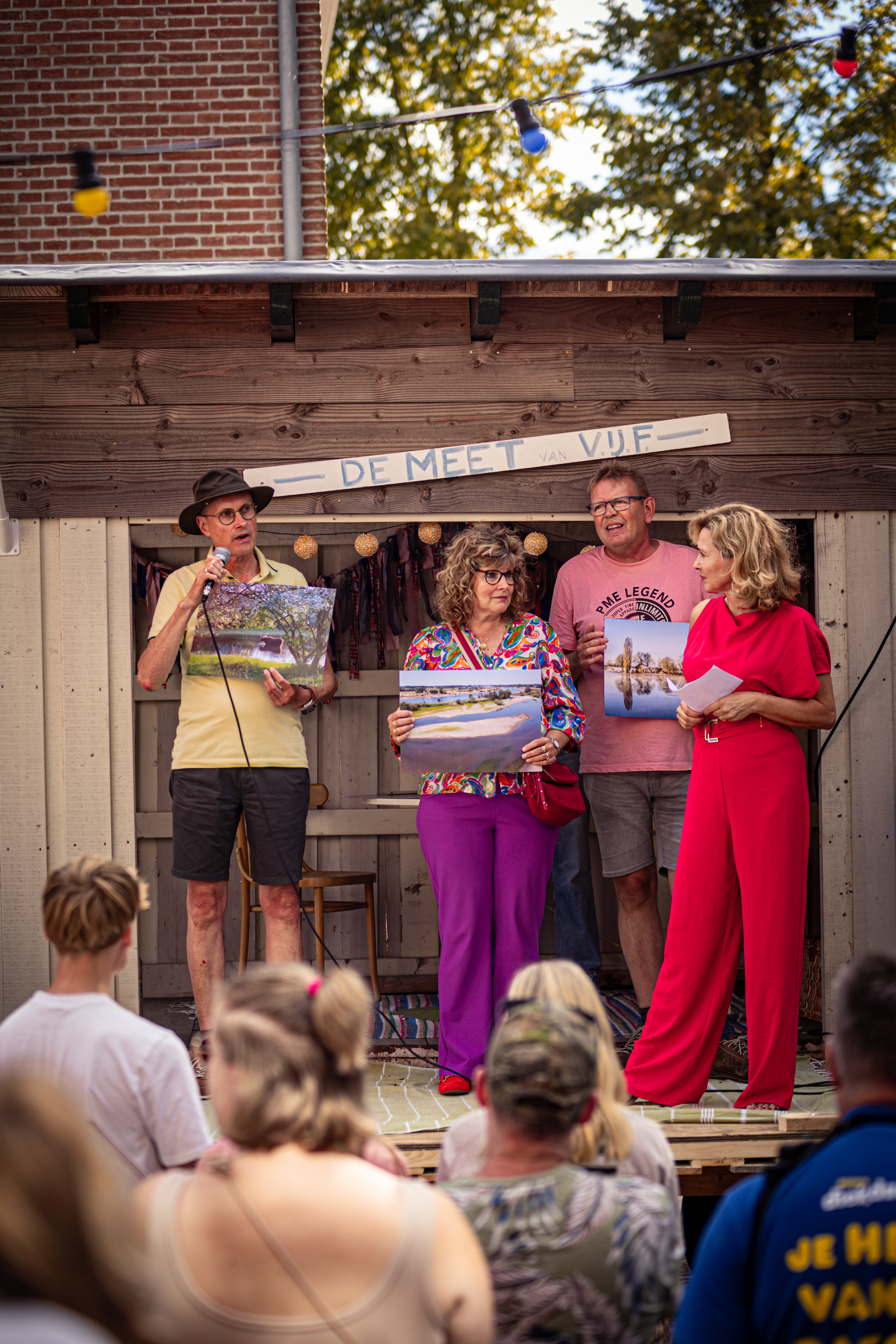Four people on a wooden stage in front of a sign that reads "De Mee Van Vlaarderpark".