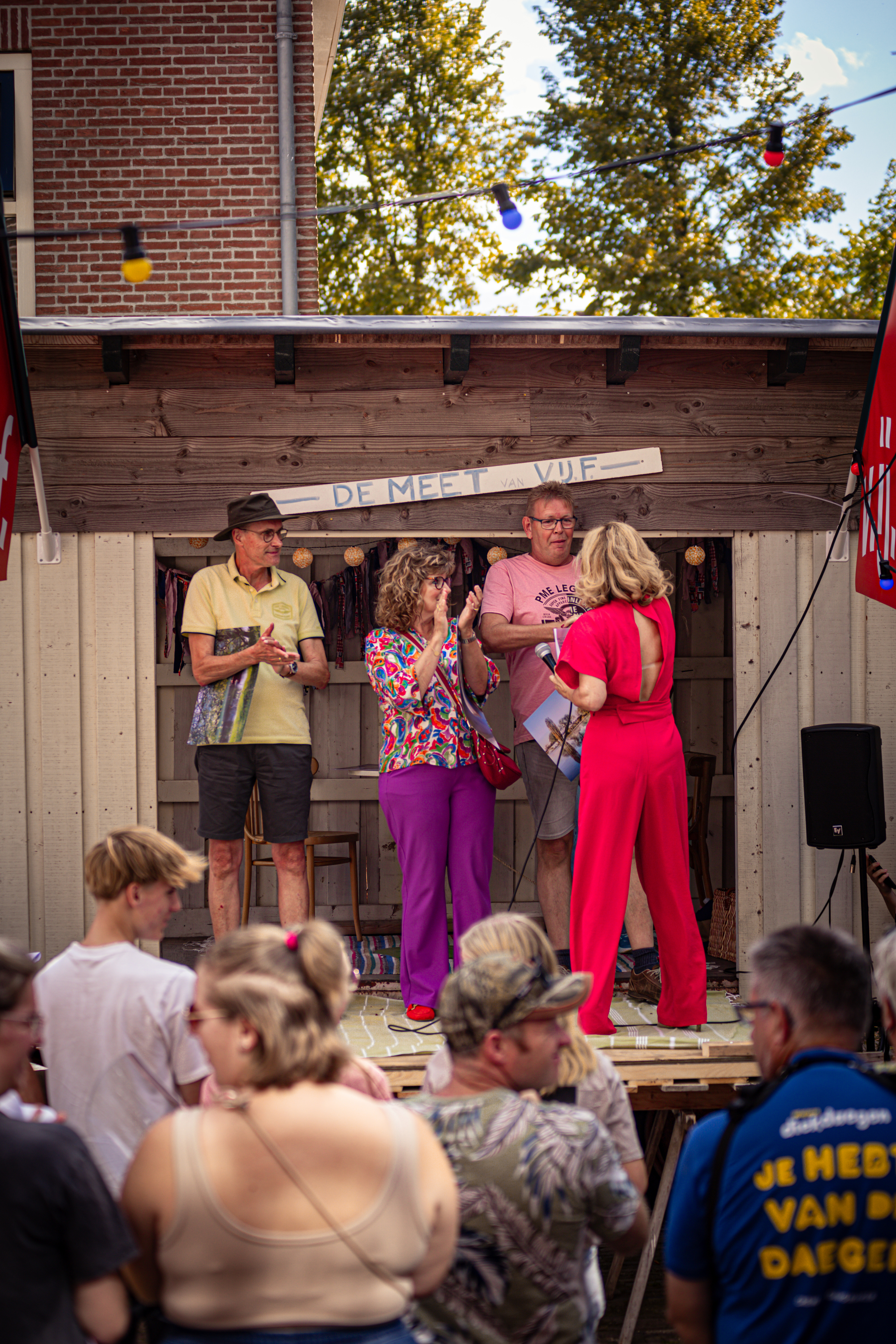 A group of people standing in front of a stage with a banner that says "We kunnen wel een beroende avond hebben".