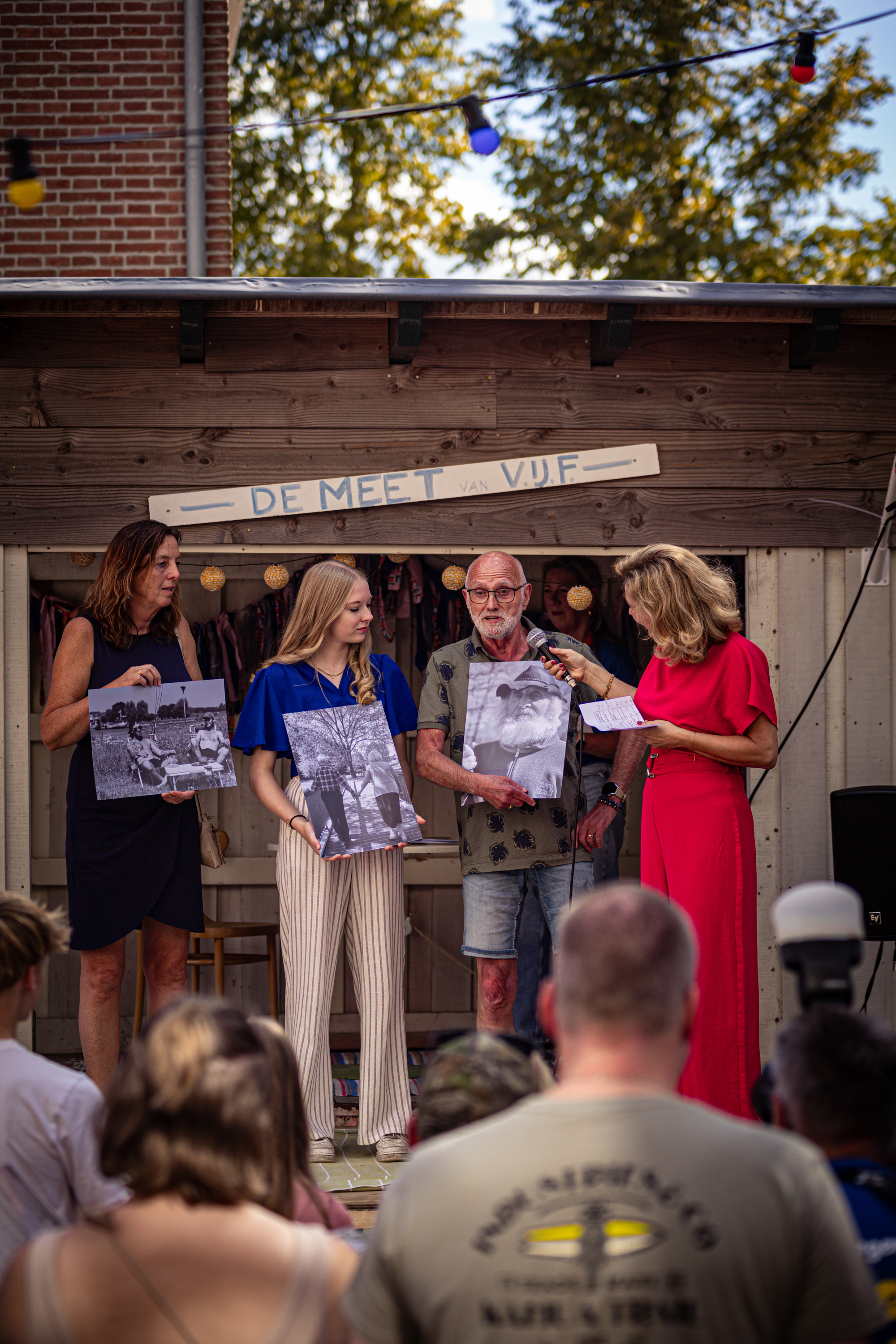 Four people standing next to each other holding pictures. The person on the far left is wearing a black dress.