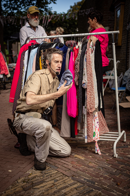 A man kneeling next to a rack of clothing outside.