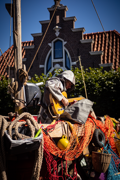 A man in a grey hoodie is playing guitar on a dock with fishing net and balloons.