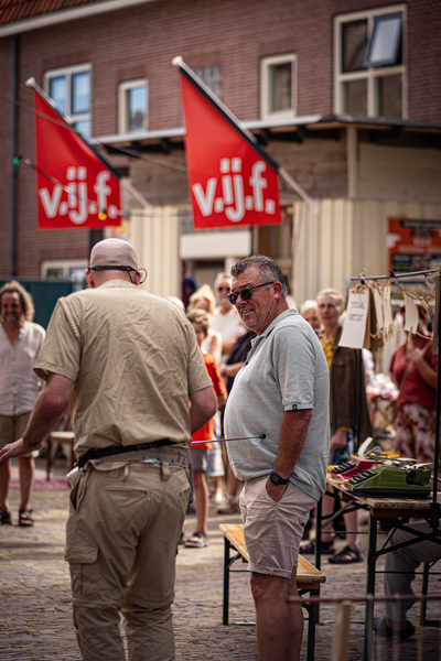 A man is standing next to a table at the V.I.J.F. Festival, with several other people behind him.