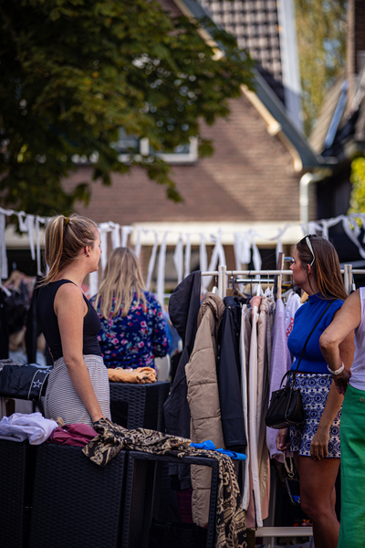 Two women are standing in front of a display of clothes at an outdoor festival.