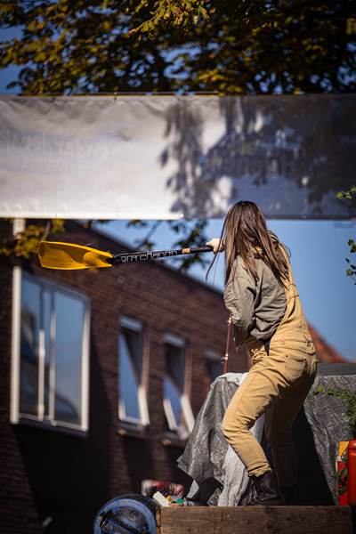 A woman in a jumpsuit is holding a yellow sign with the words "V. J. F." on it.