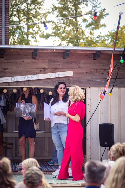 Two women in red and white attire speak on stage at the V.I.J. Festival, drawing a crowd of onlookers.