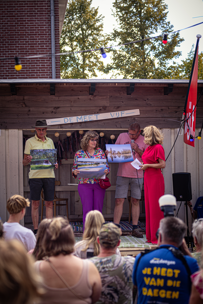 A woman is on stage at the V.IJ.F Festival, holding a photo and surrounded by people.