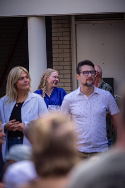A man is walking past a group of three people on a sunny day at the V.J.F. Festival.