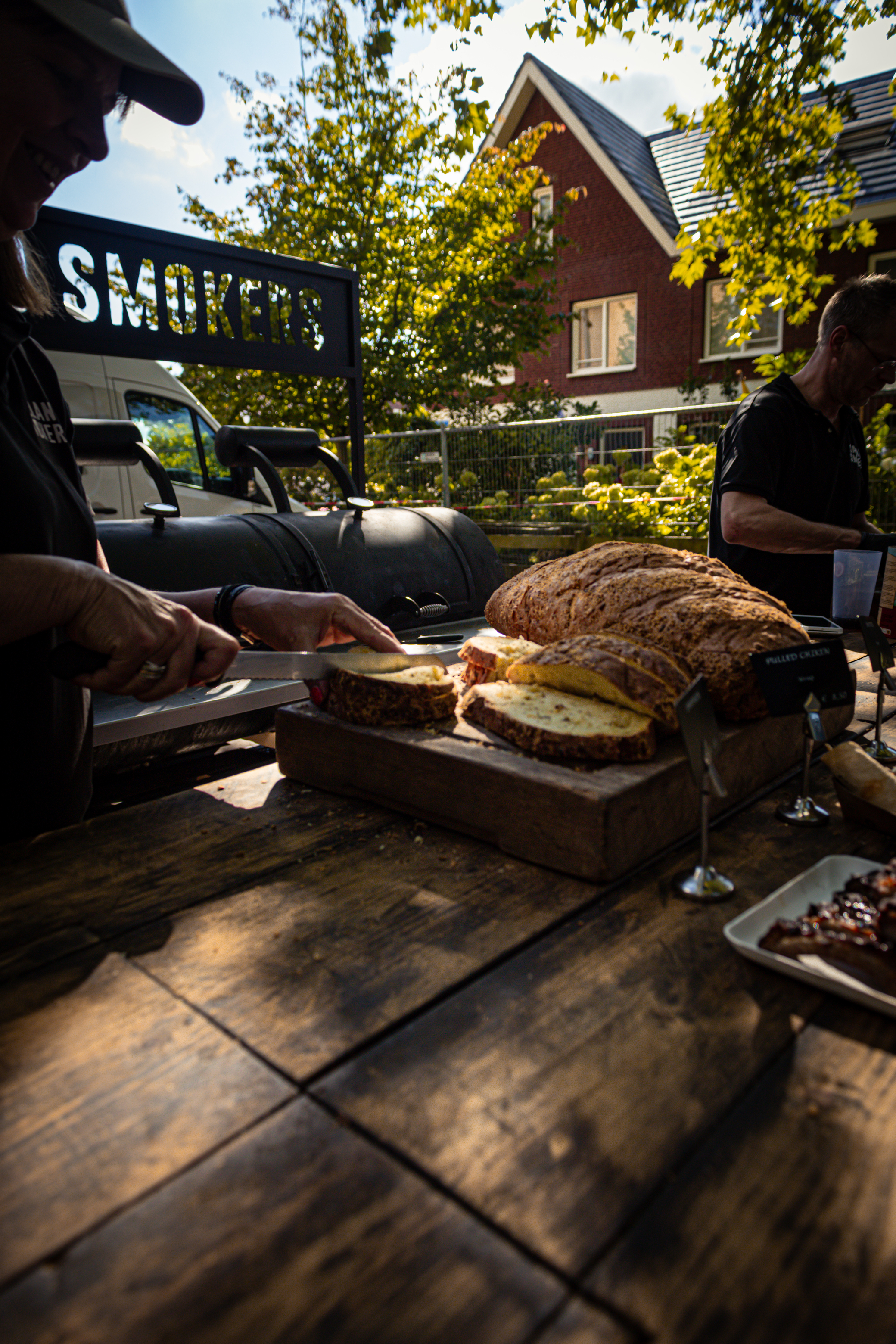 A woman is slicing a loaf of bread at a stand that sells sausages.