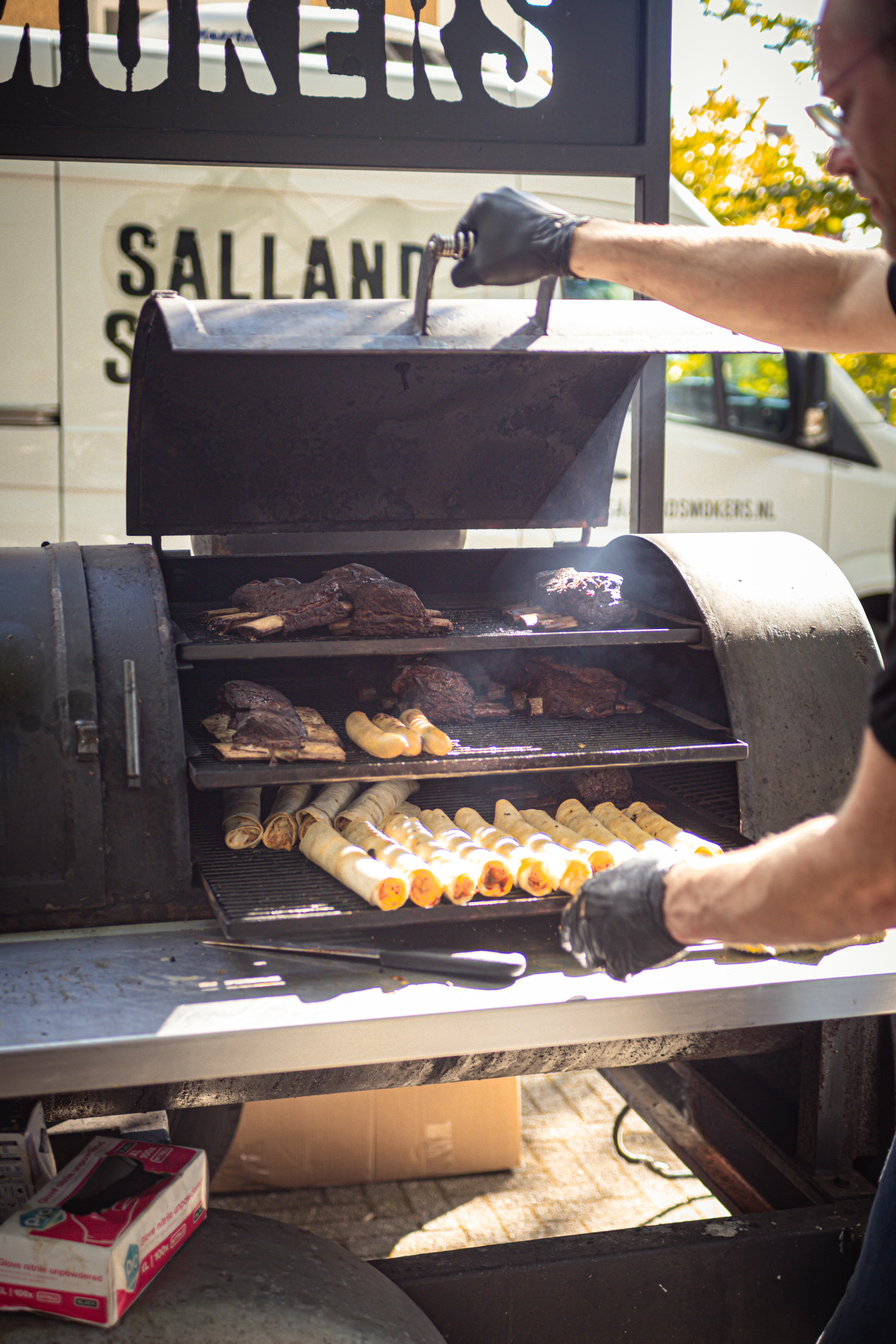 Een man in een park met een BBQ grill en hamburgers.