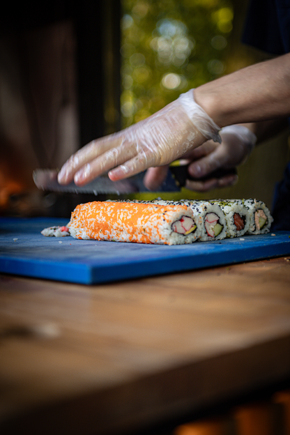 A person is preparing sushi on a cutting board in a park.