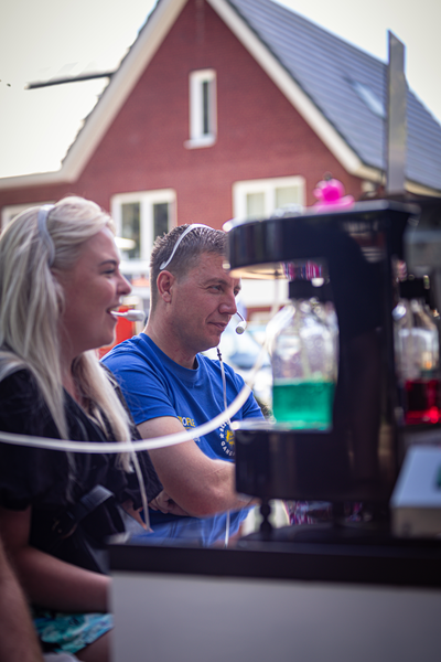 Two people standing in front of a machine with bottles inside it, one is wearing a blue shirt and the other has blonde hair.