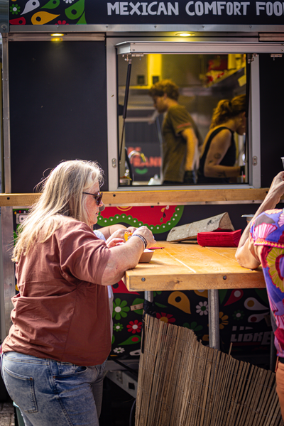 A woman wearing sunglasses ordering food at a Mexican Comfort Food stand.