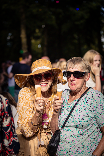 Een oude en een jonge vrouw in de zon, dragen een parasol en houden ijscreamjes.