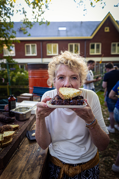 An elderly woman is eating a sandwich in front of a brown building.