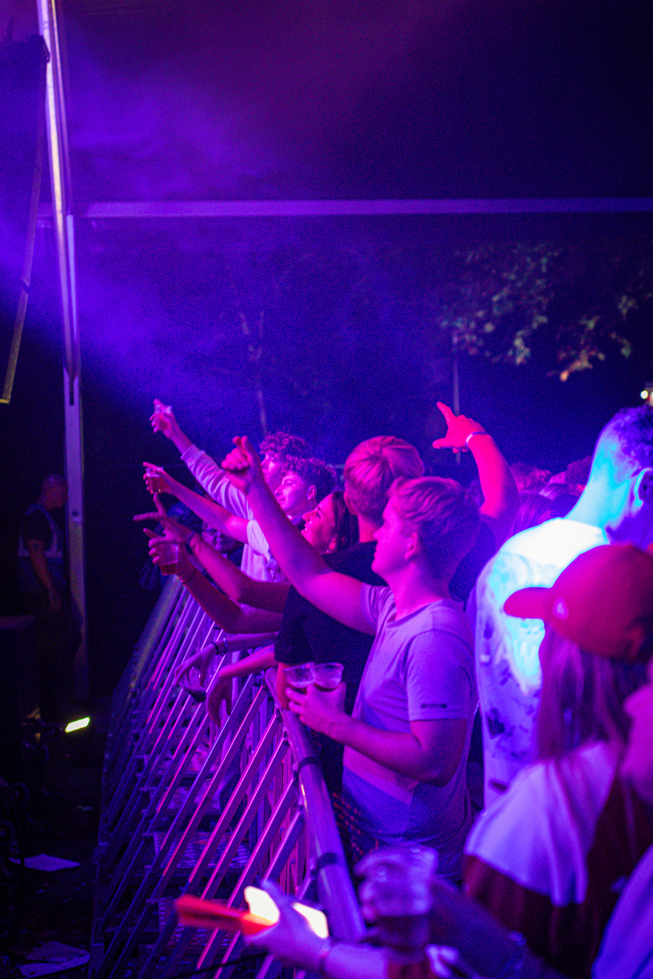 A group of people standing behind a fence at an event with purple lighting.