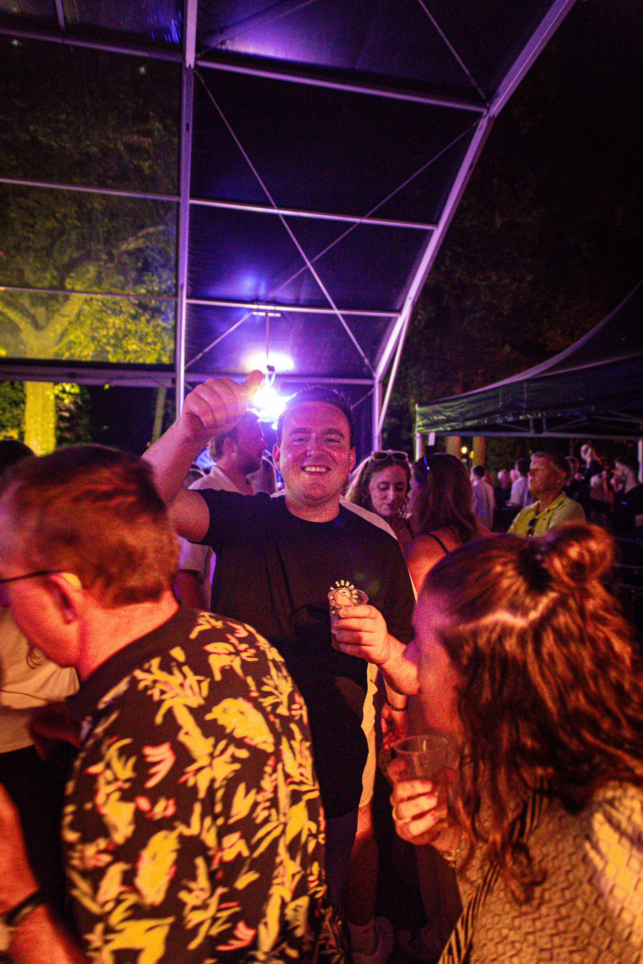 A man is raising his hand in the air at a party, surrounded by others.