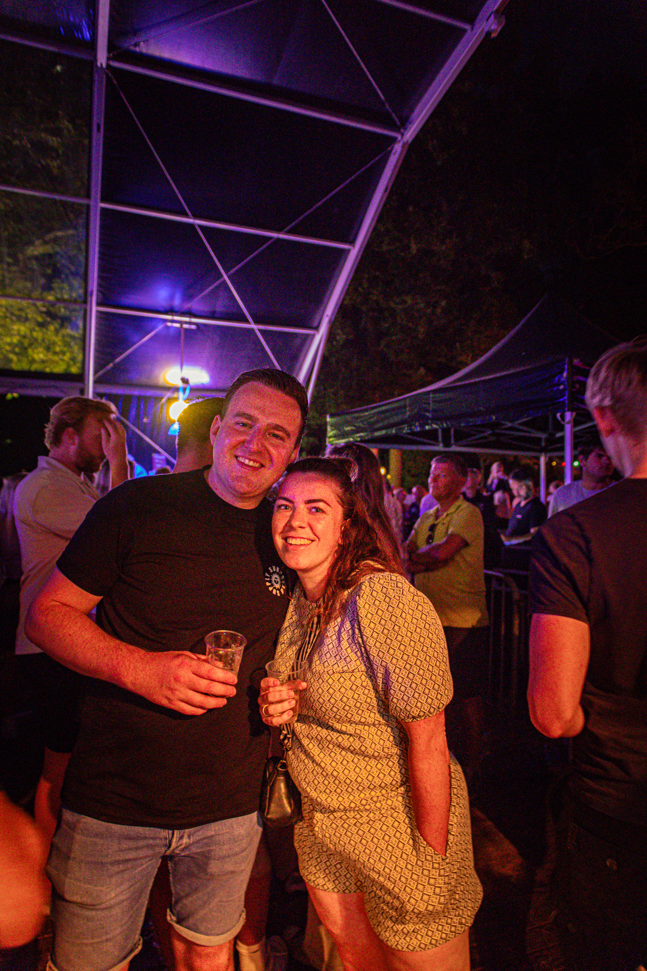 Two people pose for a photo on a night at an outdoor event.