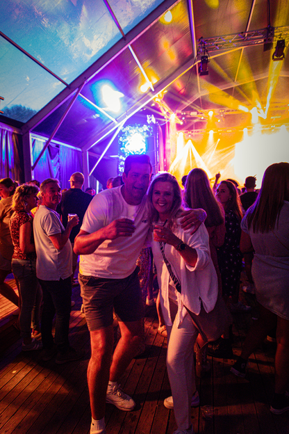 "Two people posing for a photo at the Zondagavond event, with lights and other attendees in the background."