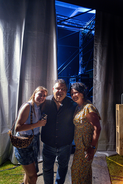 Three people stand in front of a blue lighted tent.